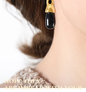 Elegant gold earrings with black teardrop pendants worn by model to show scale
