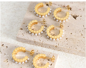 Detail view of gold C-shaped earrings with faux pearl inlay and hollow wave design