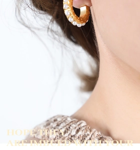 Macro side view of gold C-shaped earrings with faux pearl inlay worn on model's ear