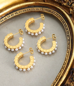 Detailed view of C-shaped gold hoop earrings with small white pearls on a vintage background
