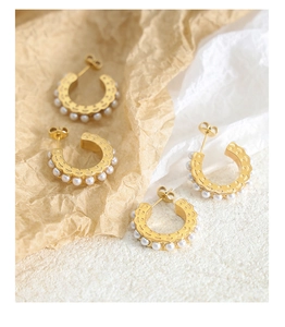 Detailed close-up of C-shaped gold pearl earrings on vintage textured paper background