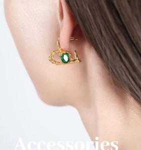 Detail of molten gold heart earring with a deep green oval gemstone on ear