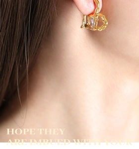 Macro view of gold heart drop earring with a clear cubic zirconia on a female model
