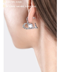 Macro shot of silver lava-style heart earring featuring a clear oval crystal on model