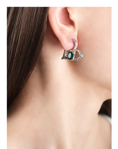Close-up of heart-shaped silver earrings with green oval stone worn by a model