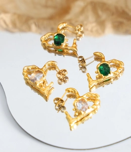 Detail of heart-shaped gold earrings with green and white gemstones on a mirror surface
