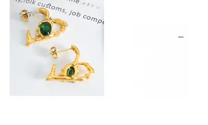 Macro detail of gold heart earrings with green oval stone and lava texture finish