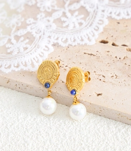 Detailed close-up of 18K gold-plated earrings with blue gemstone and white pearl on stone