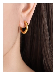 Detail shot of 18k gold plated hoop earring with star engraving and zircon on a model ear