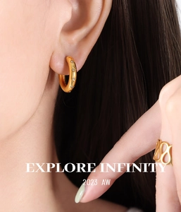 Detail of gold hoop earrings with star engravings and a geometric cutout ring on a model