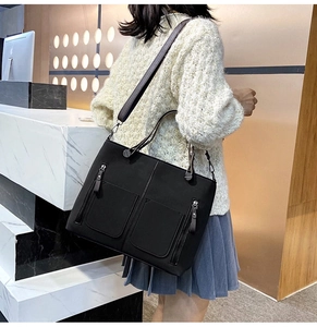 Detail view of black matte tote bag with dual front pockets and metal zippers worn by model