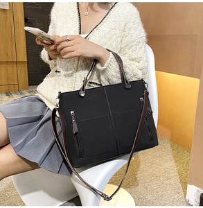 Detail of black faux leather tote bag featuring two front pockets and brown handles