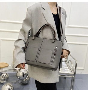 Model wearing a gray matte leather tote bag with double pockets and silver metal zippers
