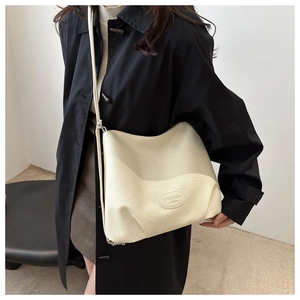Detail of the cream textured leather tote bag showing the oval fashion logo and soft pleats