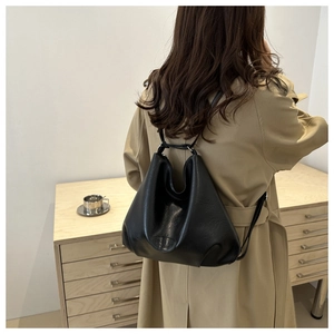 Detailed texture of black leather tote backpack shown against a classic khaki trench coat