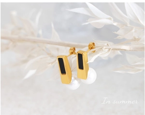 Detail of vintage gold pearl earrings with black enamel on a minimalist white branch