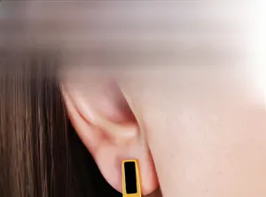 Macro view of minimalist black and gold rectangular earrings worn by a model