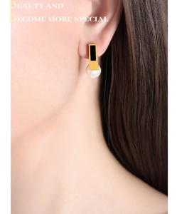Close-up of a model wearing geometric gold pearl earrings with black enamel accents