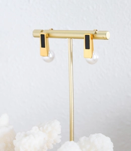 Detail of gold rectangular earrings with black enamel and dangling round white pearls