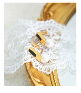 Detailed close-up of retro gold earrings with black enamel inlay and white round pearls