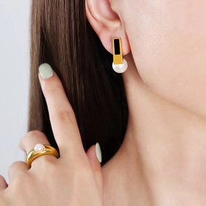 Elegant gold earrings with black enamel and white pearls shown on a female model