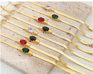 Flat gold snake chains with vibrant oval gemstones on an elegant marble surface