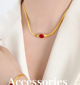 Close-up of golden snake chain jewelry set with red oval stones worn on a white suit