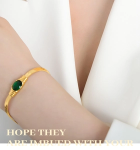 Close-up of gold snake chain bracelet featuring a large oval green gemstone on a model