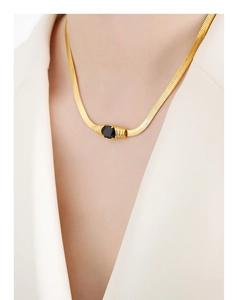Macro view of gold snake chain necklace featuring a claw-set oval black stone on a model