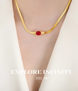 Close-up of a gold snake chain necklace with an oval red zircon stone on model