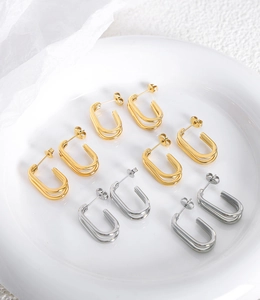 Dettaglio di orecchini geometrici minimalisti in oro e argento su un vassoio di ceramica