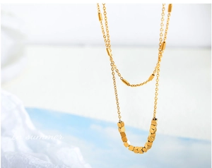 Détail macro d'un collier double couche doré avec cubes géométriques et cylindre