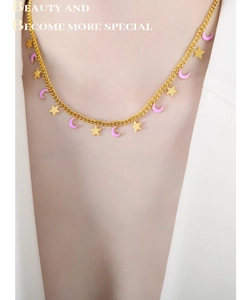 Dettaglio della collana stella e luna dorata con smalto viola su sfondo abito bianco