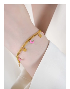 Dettaglio di un bracciale con stella dorata e luna in smalto rosa sul polso