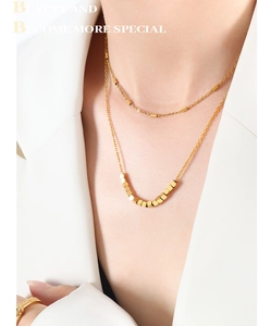 Gros plan du collier double épaisseur doré avec pendentif cube sur costume blanc