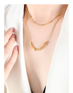 Détail d'un collier double épaisseur doré avec perles géométriques porté par un mannequin