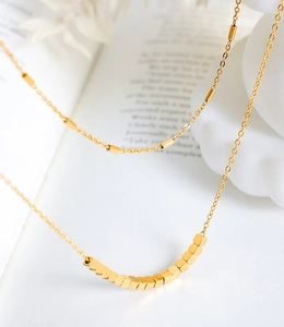 Détail de perles dorées carrées et franges sur un collier à double rangée minimaliste