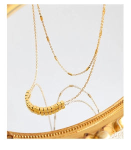 Détail d'un collier double rang en titane doré avec cubes géométriques sur un miroir