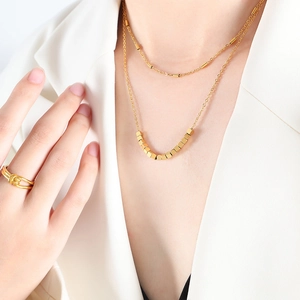 Collier géométrique doré double épaisseur et bague torsadée sur femme en blazer blanc