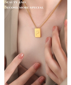 Detail of gold square pendant with engraved letter P on a dainty titanium chain