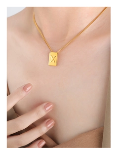 Close-up of a minimalist gold letter X square pendant necklace worn by a model