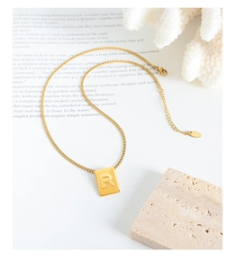 Macro shot of gold square letter R pendant necklace on a minimalist aesthetic background