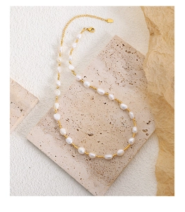 Detail of baroque pearl and gold bead necklace on a beige travertine display stand