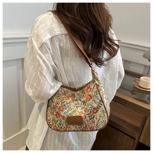 Detail of floral woven crescent bag with brown leather tag and adjustable strap