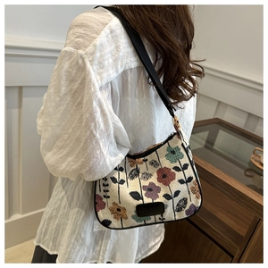 Close-up of beige fabric shoulder bag with colorful floral patterns and black leather logo
