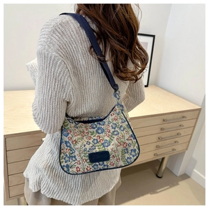 Detail of floral jacquard crescent bag with adjustable blue strap and brand label