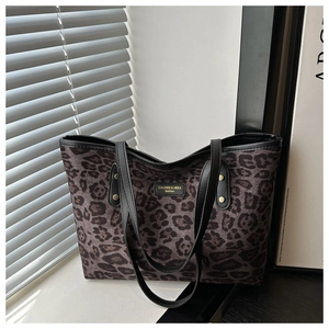 Detail of leopard print tote bag with black leather straps and brand logo patch