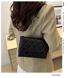Rear view of model wearing a black quilted crossbody bag with silver metal chain strap