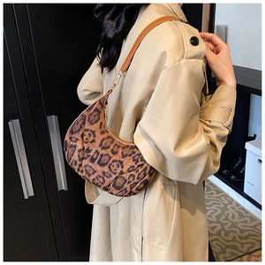 Detail of leopard print crescent bag with brown leather strap worn with a beige trench coat