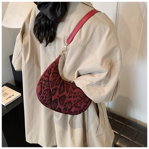 Detailed view of leopard print crescent hobo bag with red leather strap on a side table